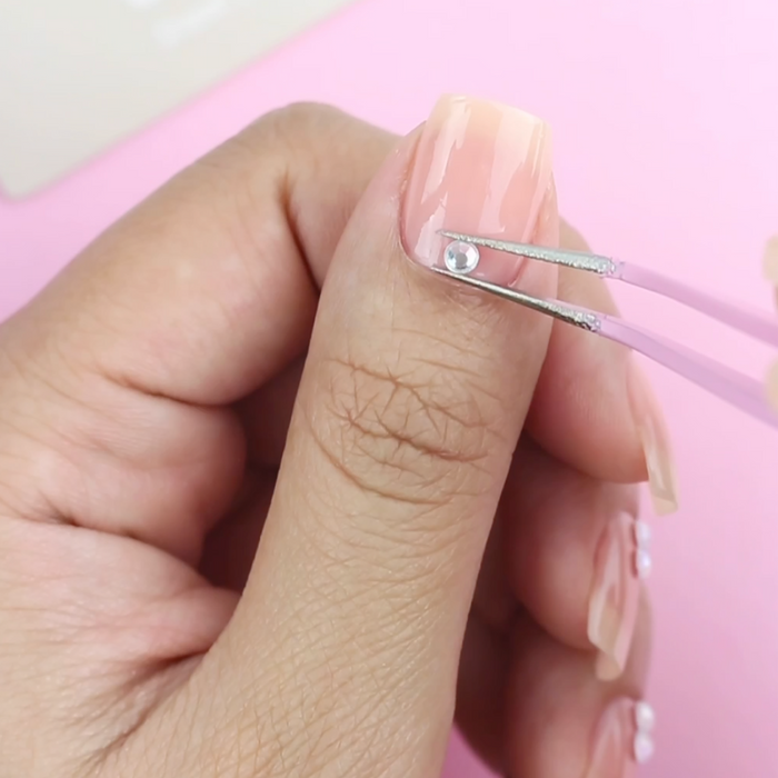 Applying a pearl decal to a sheer pink nail with the pink tweezer