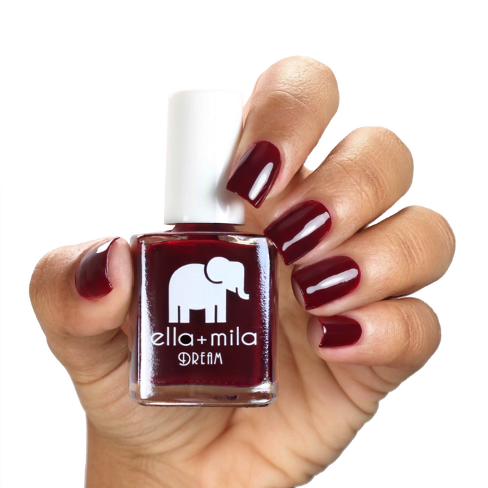 Nightdreamer dark wine red nail polish on a medium skin tone, hand holding the bottle