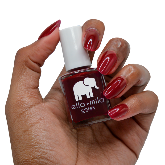 Nightdreamer wine red nail polish on a deep skin tone, hand holding the bottle