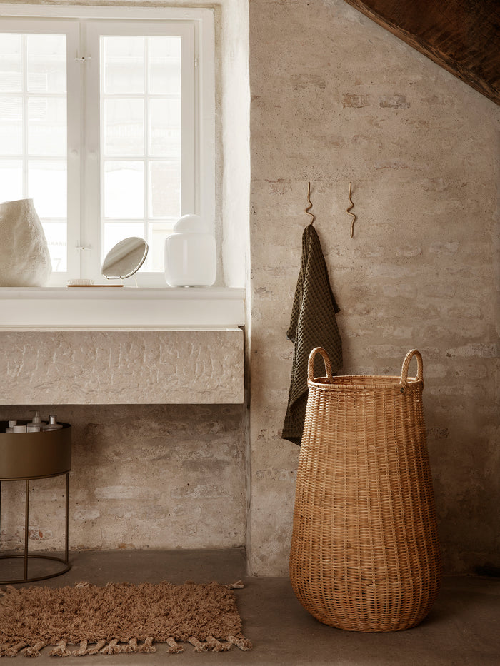 Waffle bath towel in olive hanging from a wall hook in a rustic bathroom beside a tall woven laundry basket