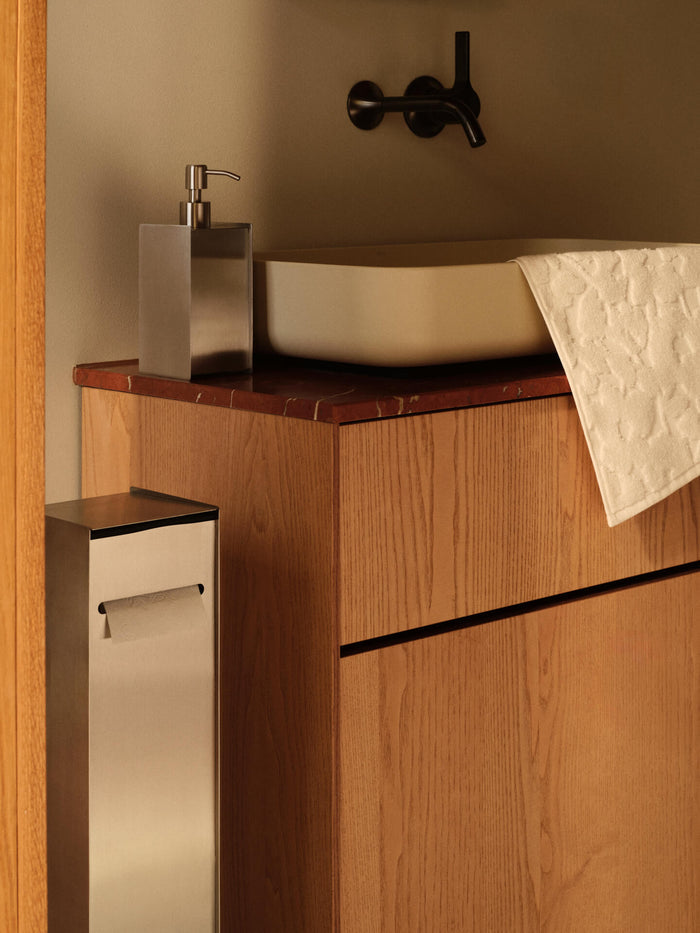 The soap dispenser on a red washbasin counter, with a matching toilet roll holder