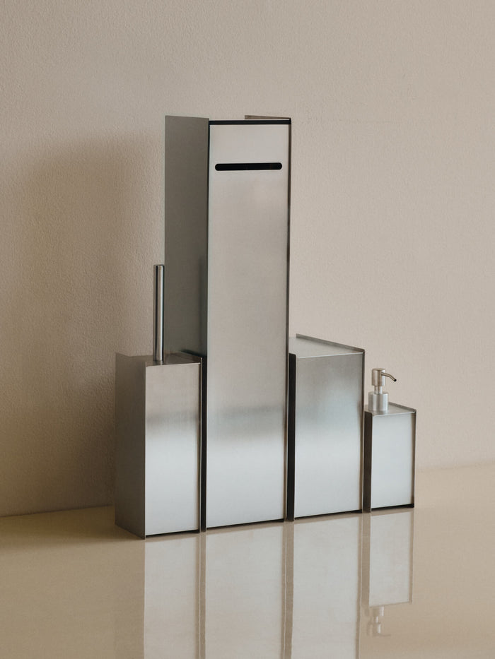 The soap dispenser lined up with a toilet brush, roll holder and bin in brushed stainless steel
