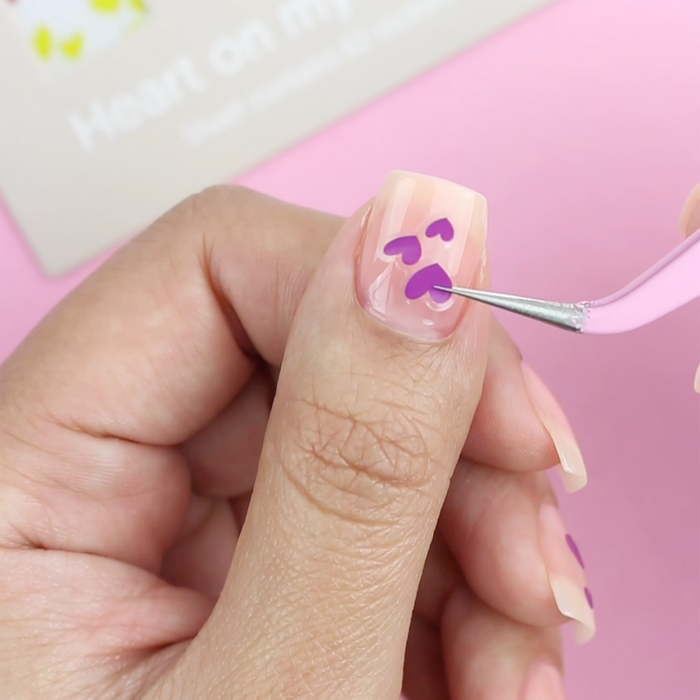 Using the pink tweezer to place a purple decal on a sheer nude nail